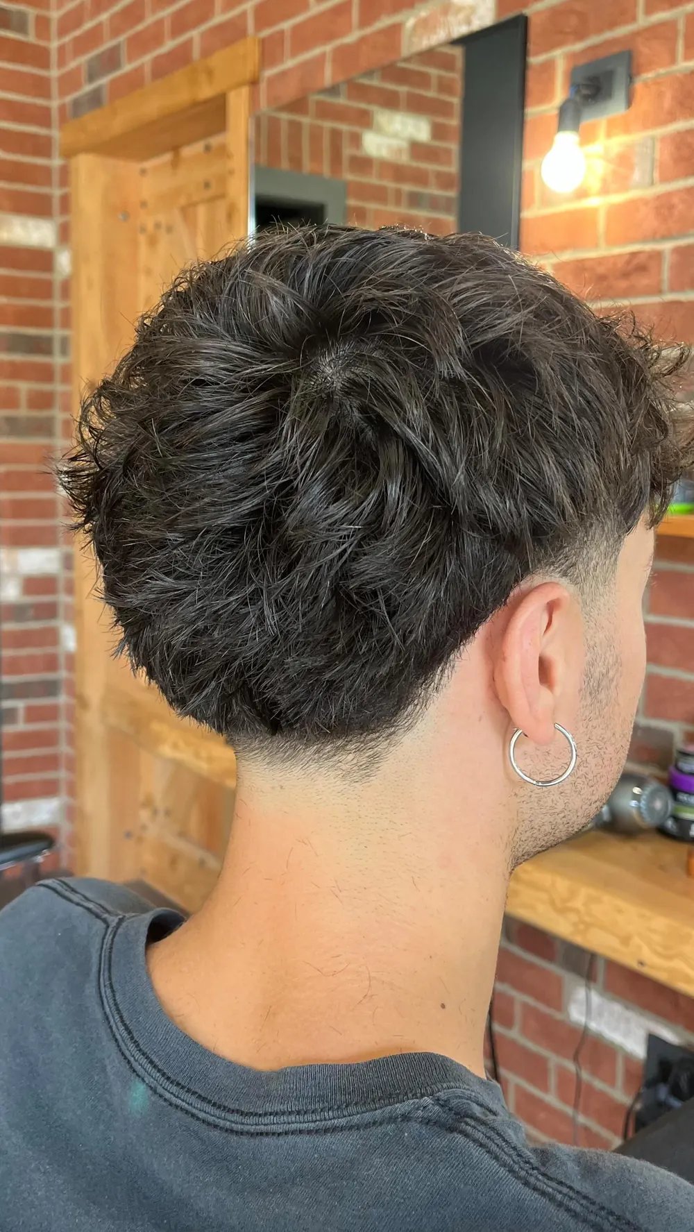 Taglio uomo corto e mosso con sfumatura, davanti al muro di mattoni del barber