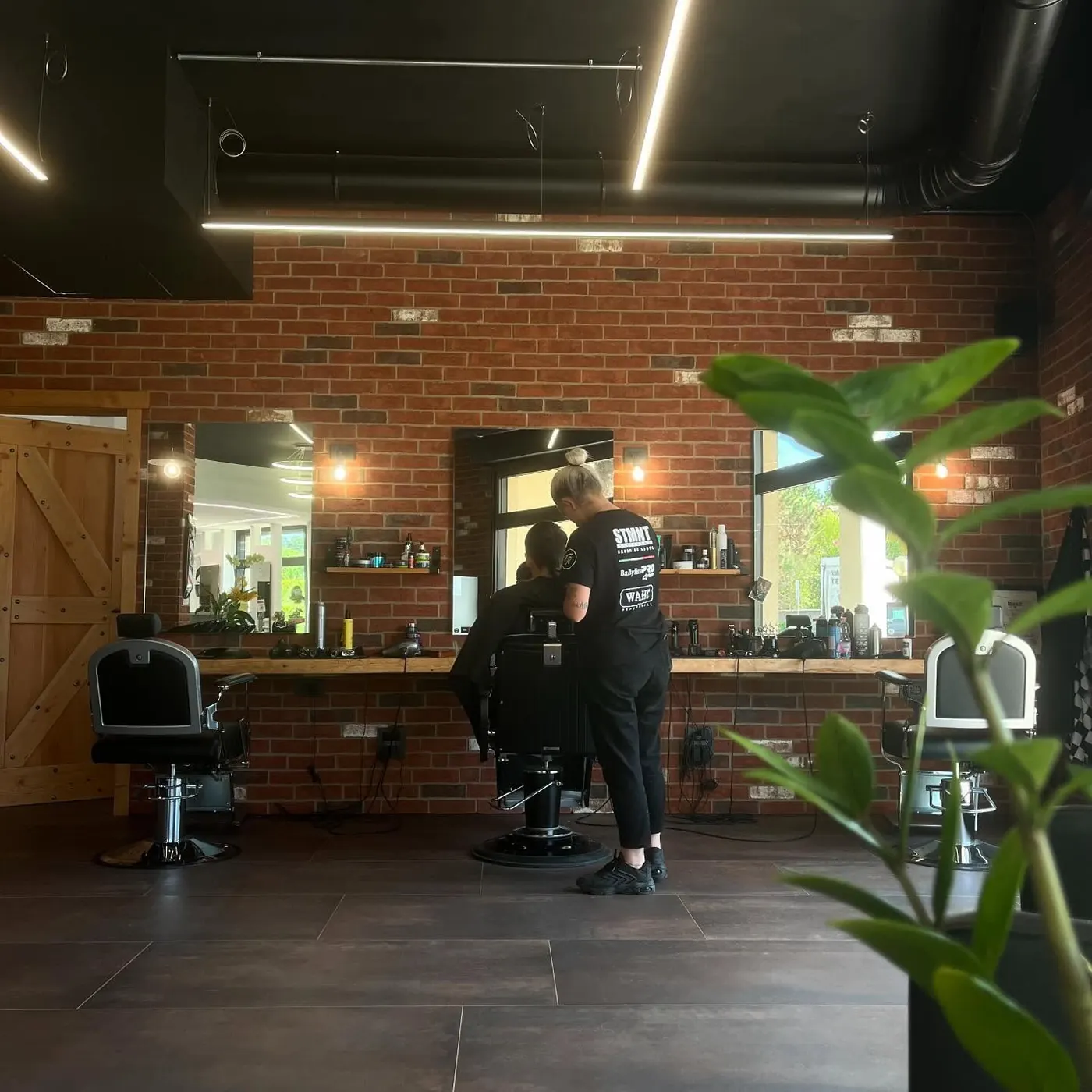 Il lato barber: muro di mattoni, specchi, poltrone nere e mensole in legno